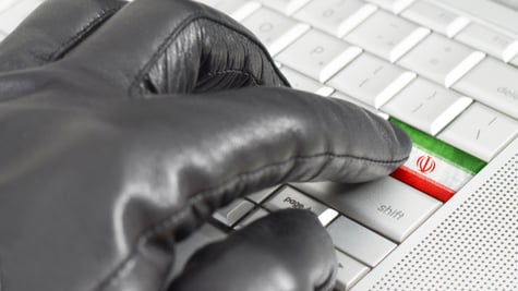 Hacking Iran concept with hand wearing black leather glove pressing enter key with flag overlaid